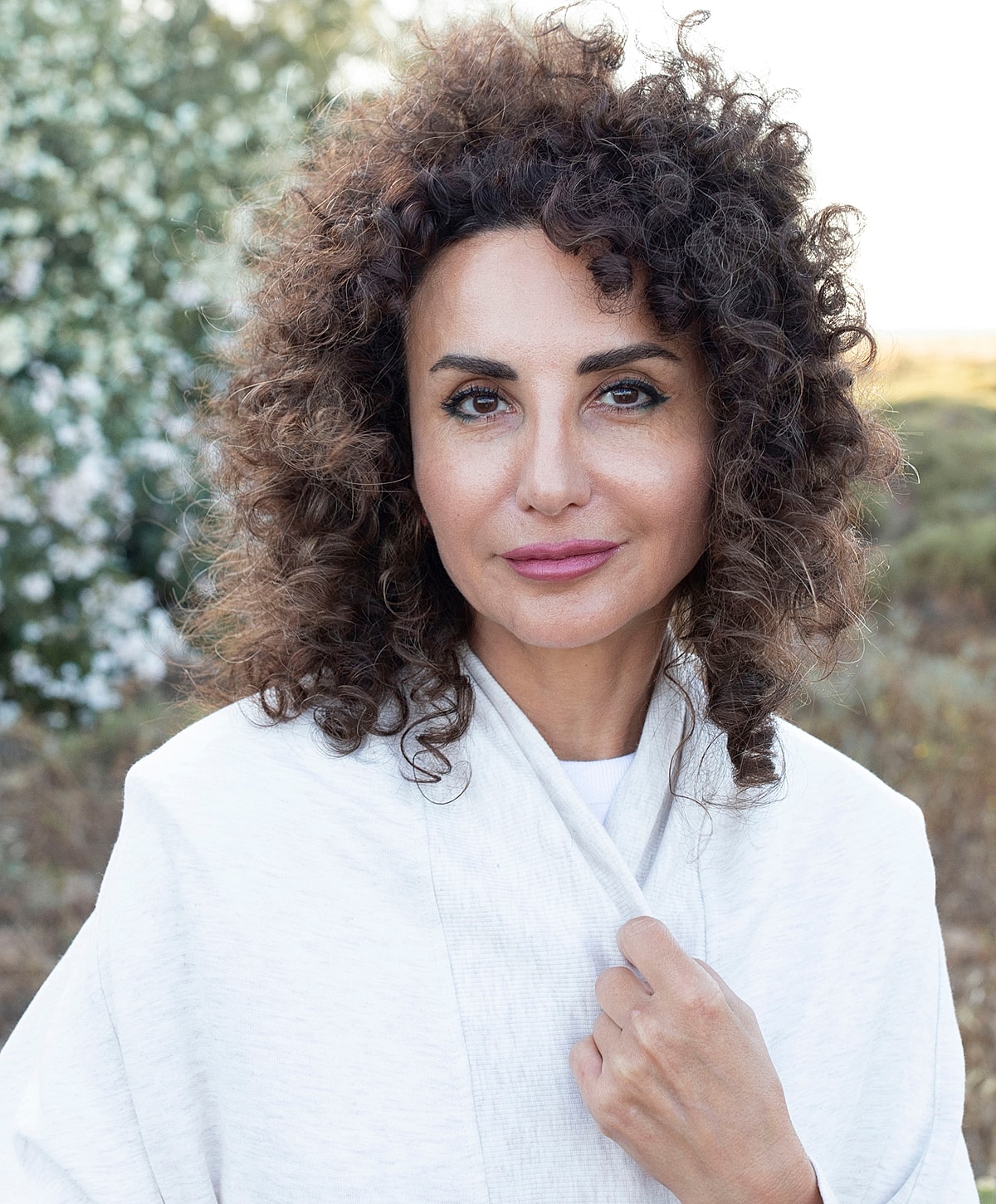 Woman with curly hair outdoors, softly smiling.