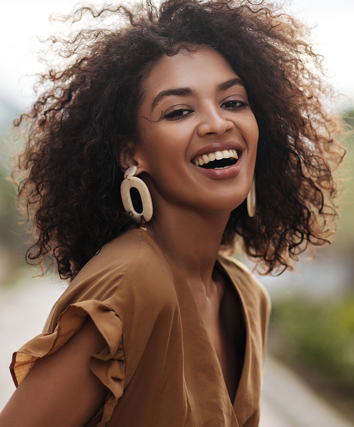 Smiling woman with curly hair and large earrings.