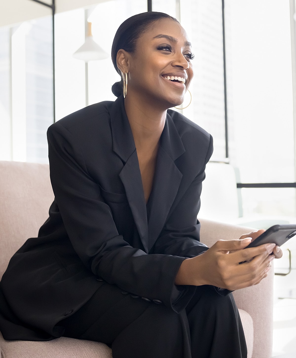 Smiling woman in black suit using smartphone.