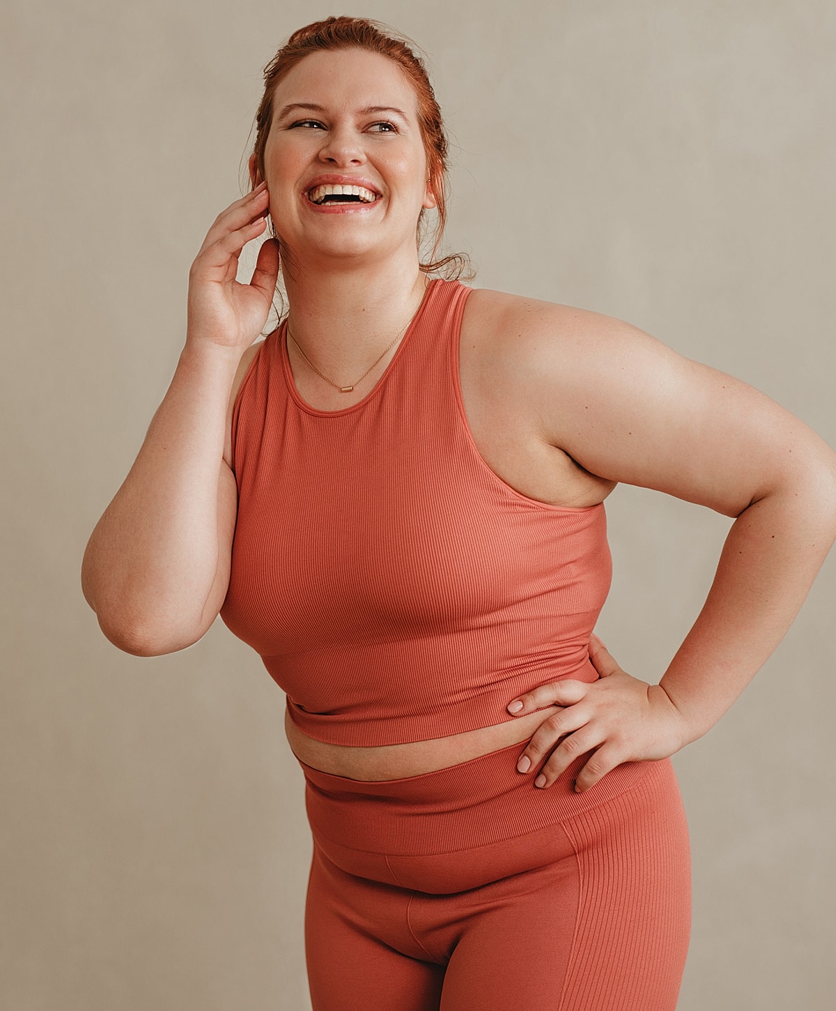 Smiling woman in athletic wear against neutral background.