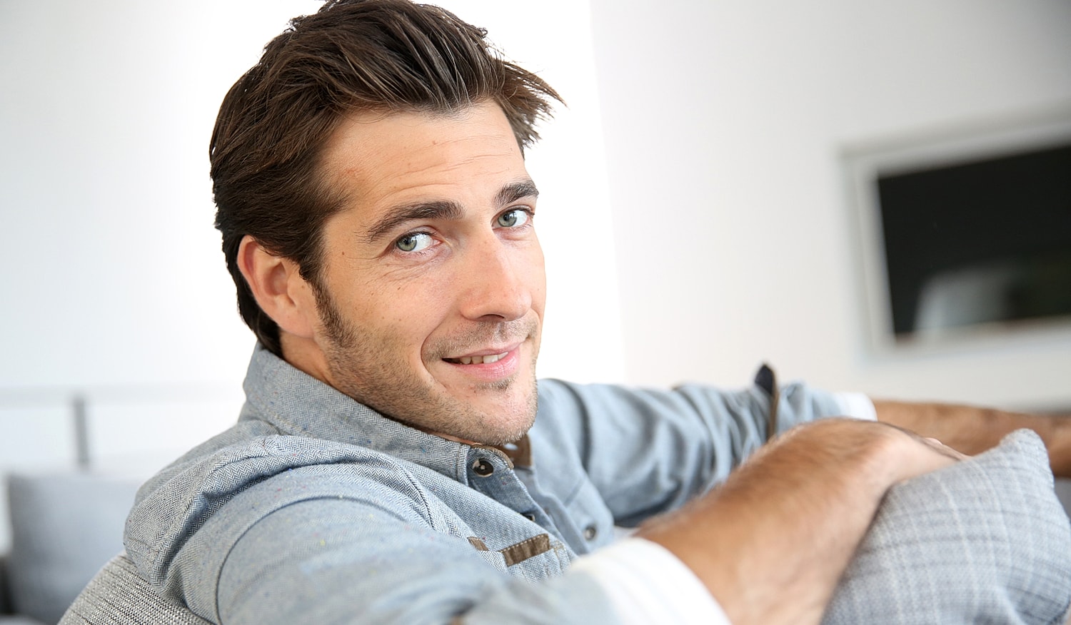 Smiling man in casual attire, relaxing indoors.