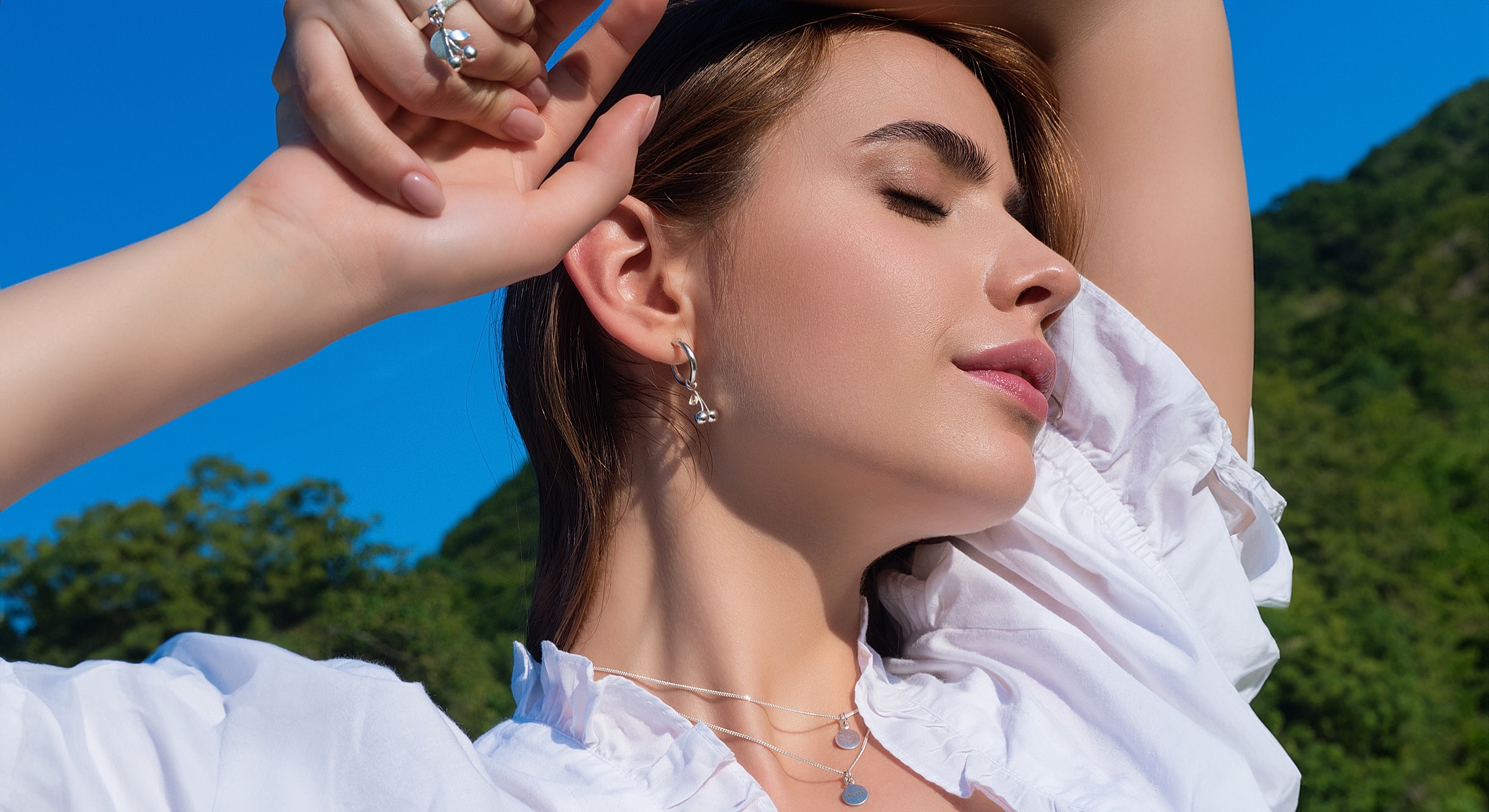 Model showcasing jewelry against a blue sky.