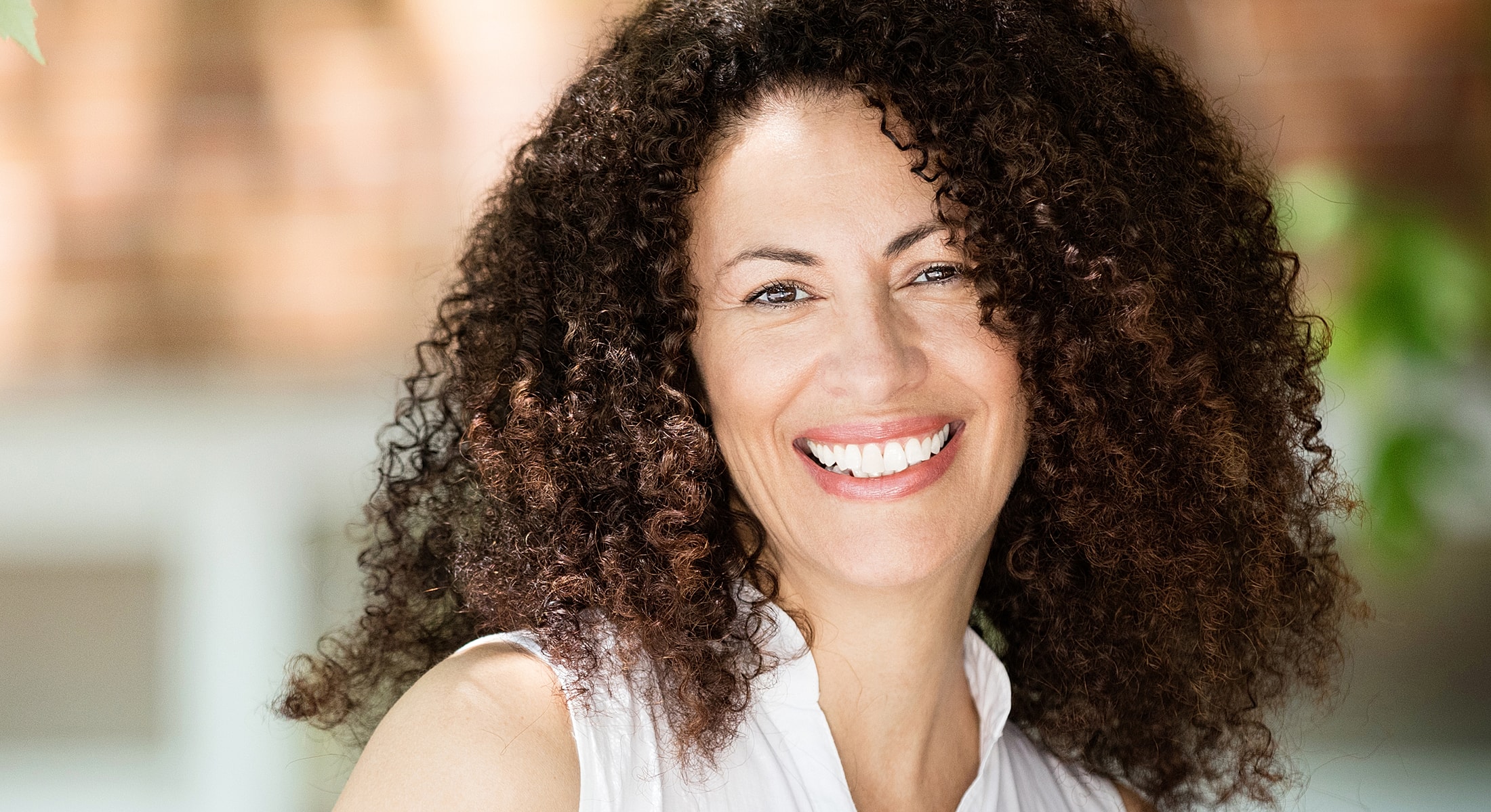 Smiling woman with curly hair outdoors.