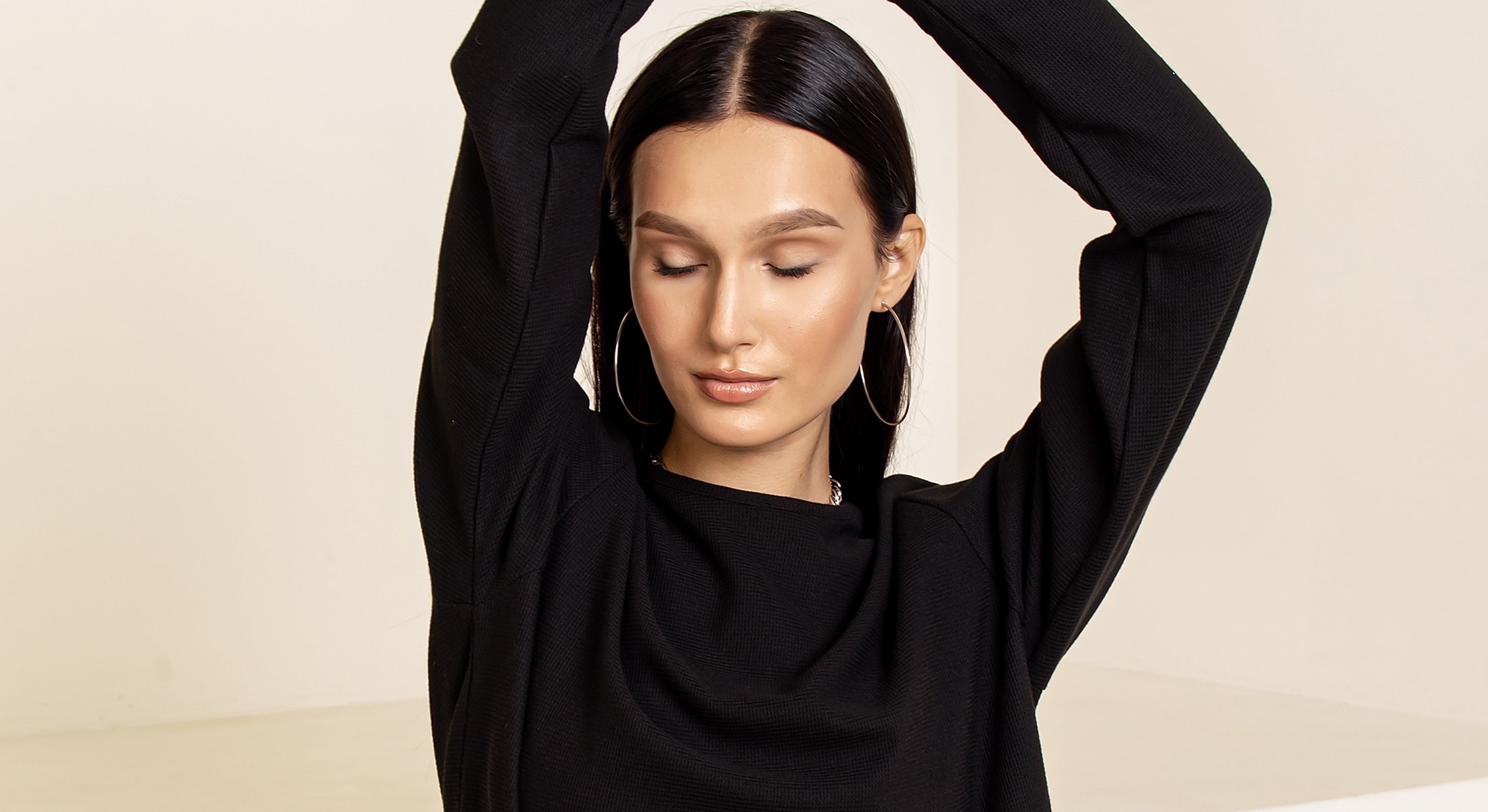 Model posing with closed eyes and raised arms.
