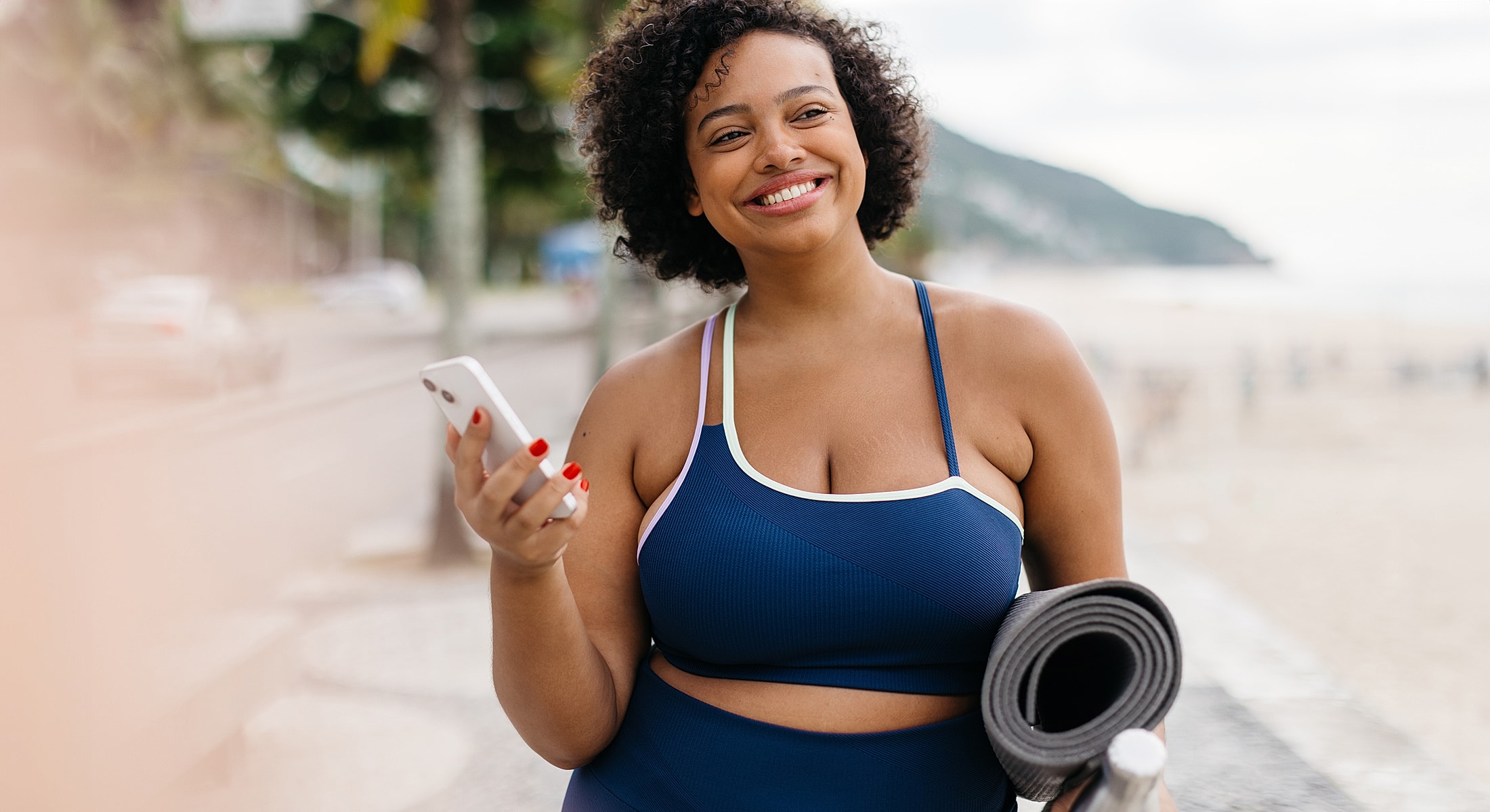 Smiling woman holding phone and yoga mat.